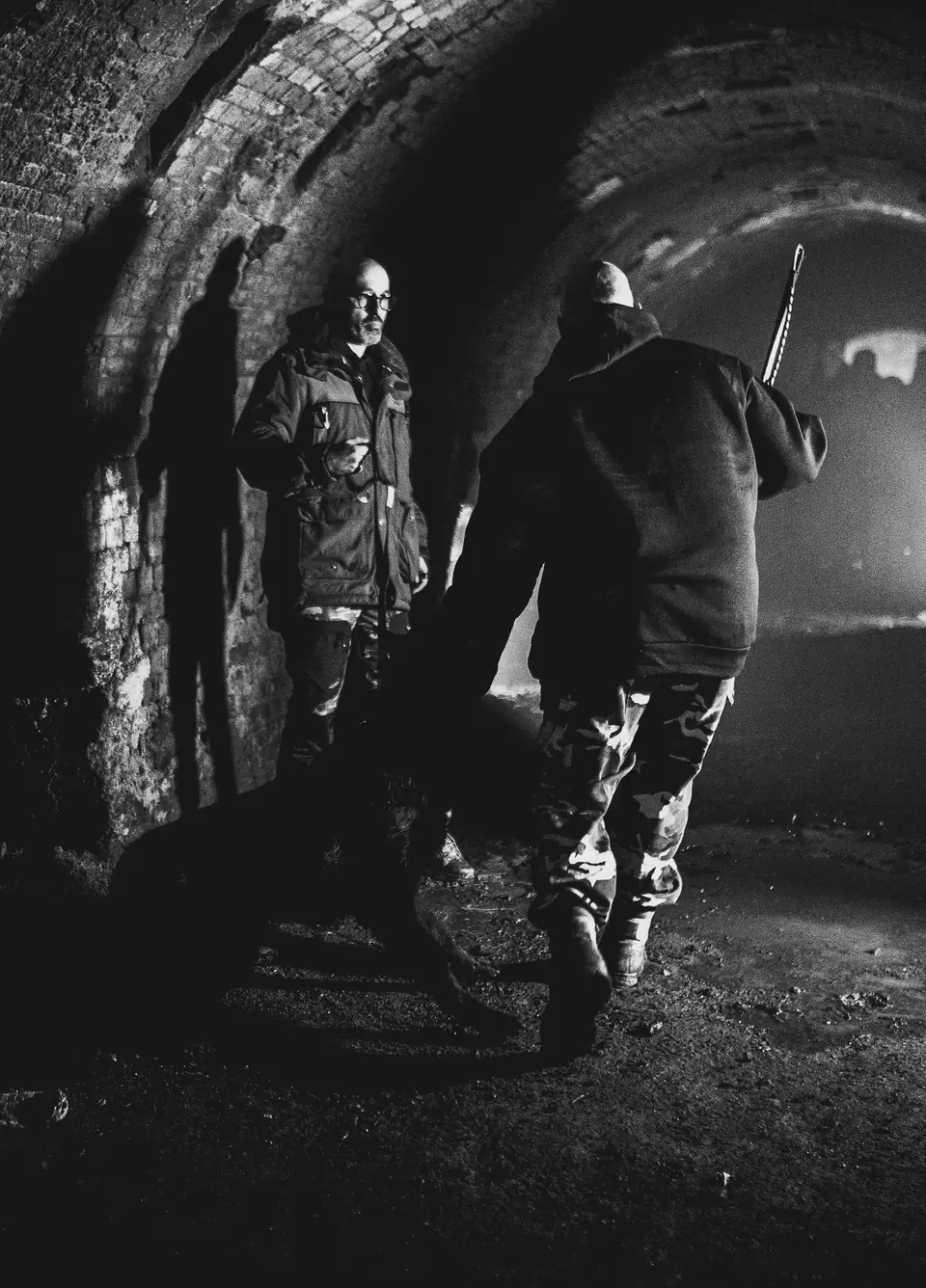 German Shepherd training with two handlers beneath a brick arch